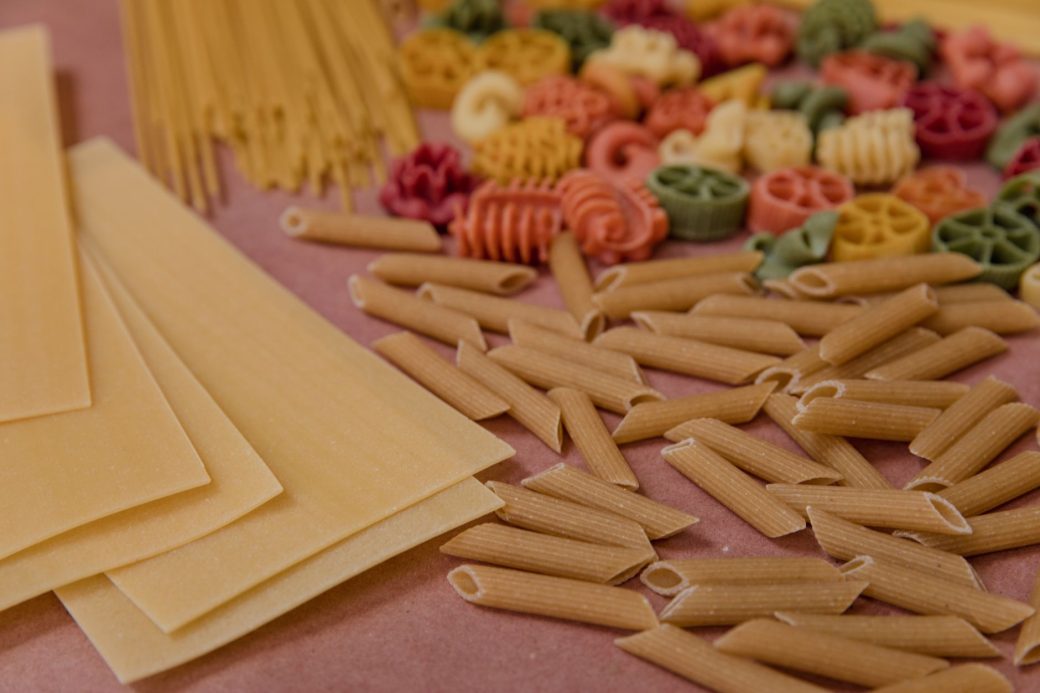 Assorted uncooked pasta varieties displayed on a wooden surface, perfect for culinary concepts.