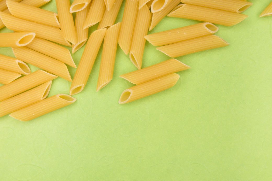 High angle shot of uncooked penne pasta scattered on a vibrant green surface.