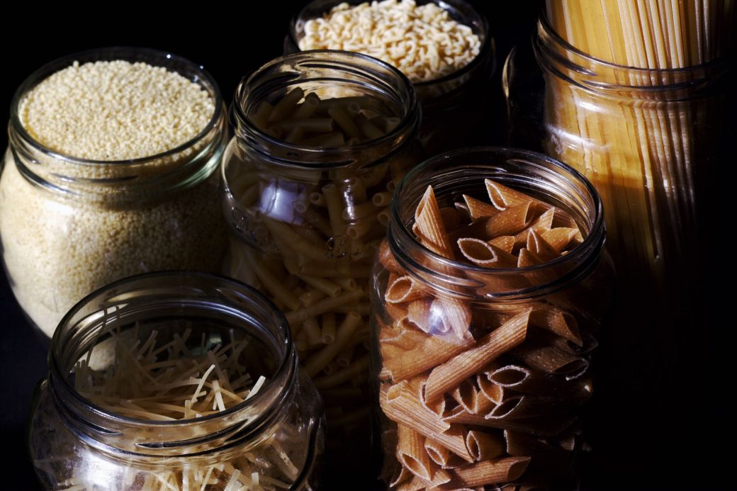 Different types of pastas and cereals in glass jars on kitchen in sunlight