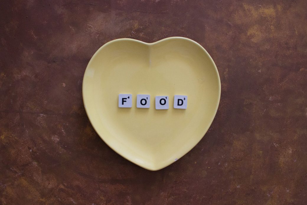 Creative arrangement of Scrabble tiles spelling 'FOOD' on a heart-shaped plate, perfect for culinary themes.