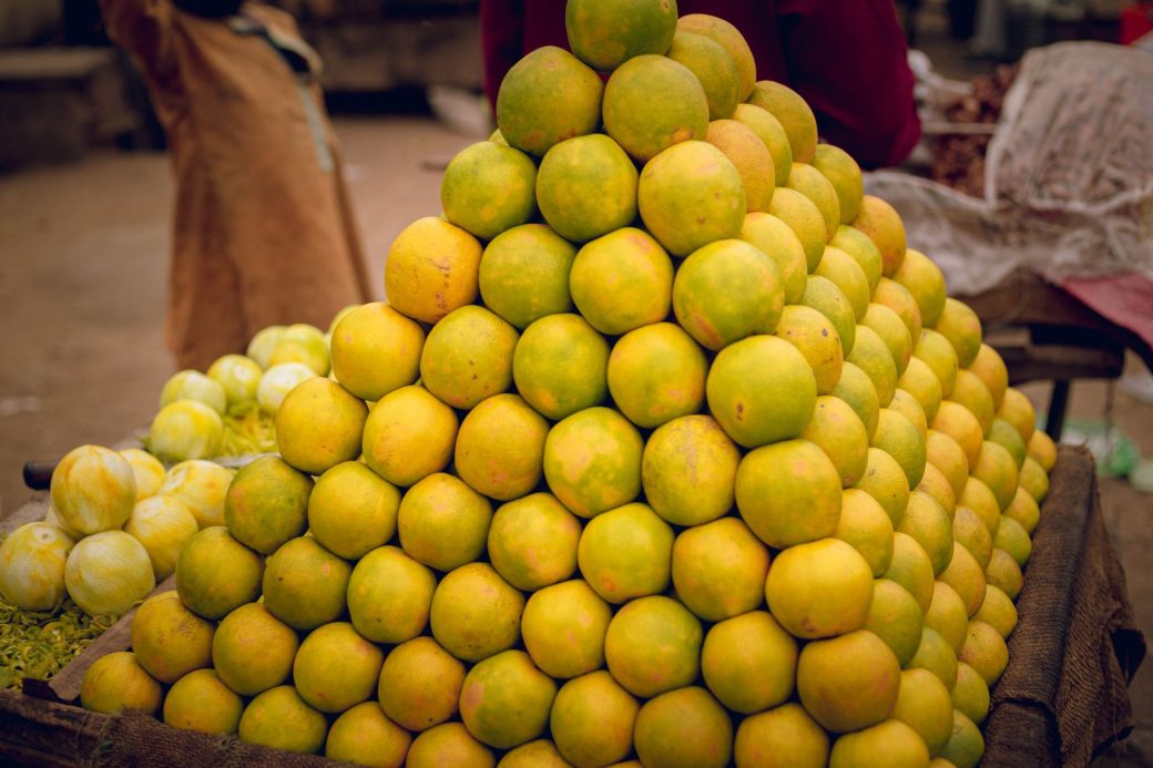 A pyramid of fresh lemons stacked at an outdoor market, showcasing vibrant colors and ripe citrus.