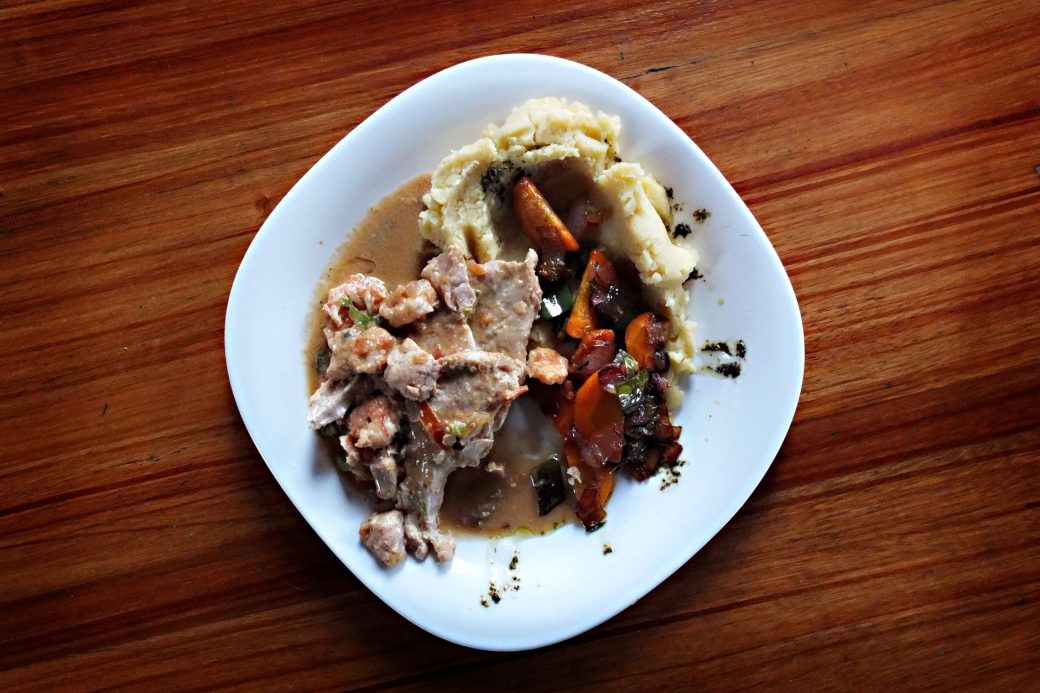 A savory dish of meat and vegetables with mashed potatoes on a wooden table.