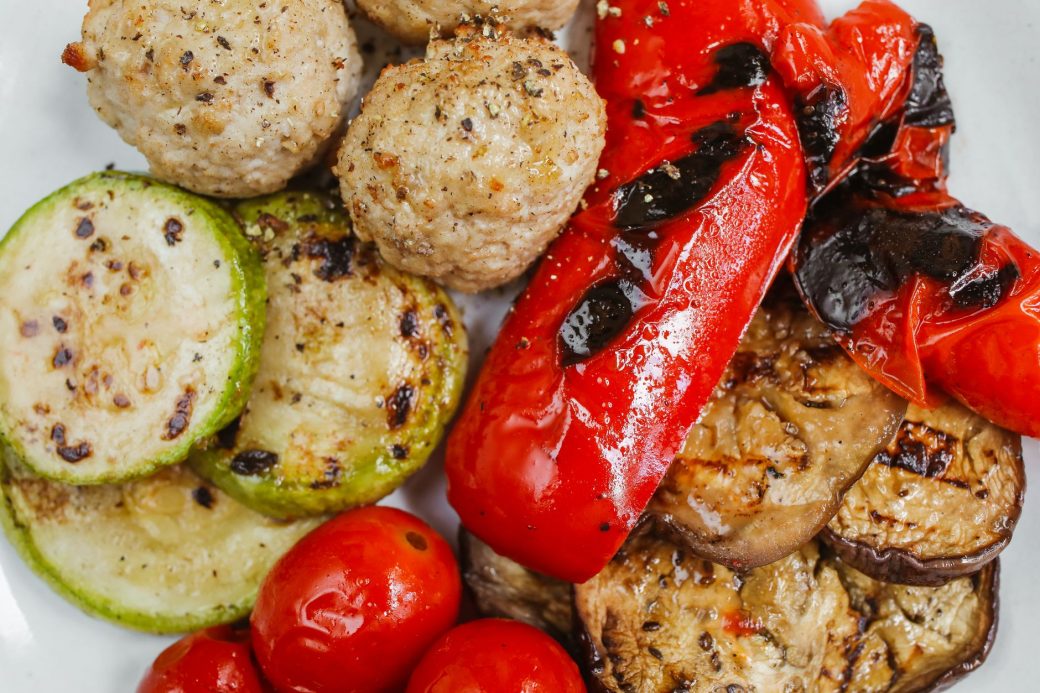 Close-up of grilled vegetables and meatballs with vibrant colors and textures.