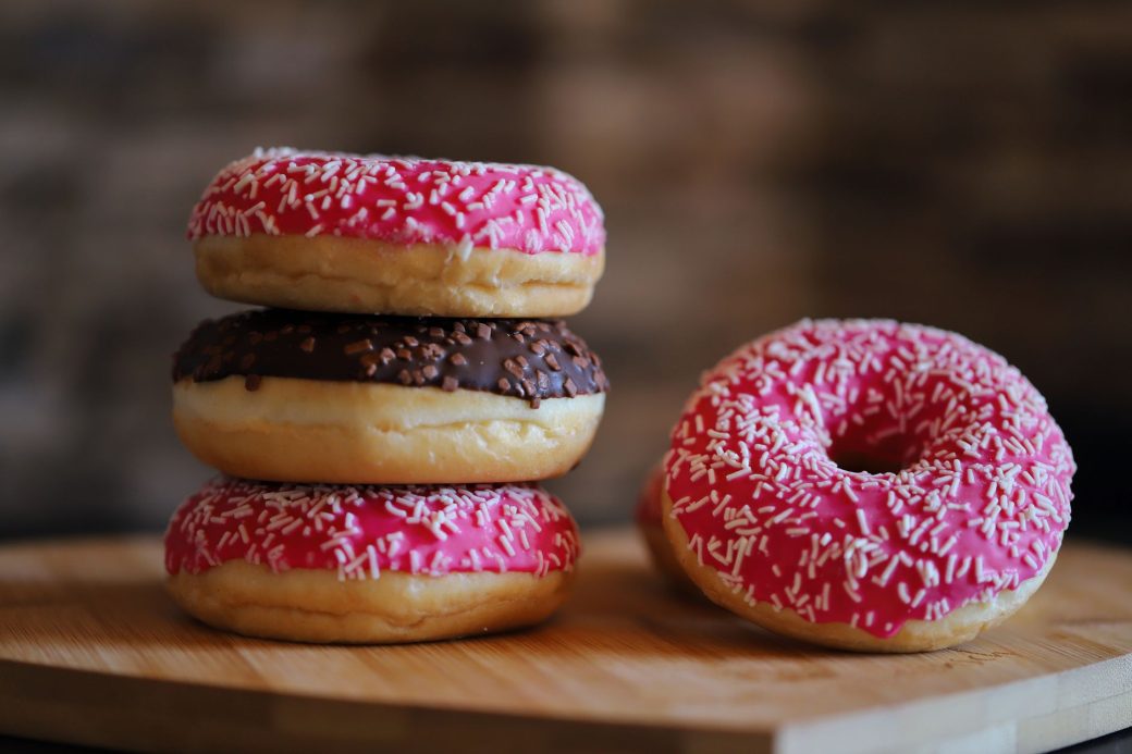Close-up of vibrant pink and chocolate frosted doughnuts with sprinkles stacked on a wooden board.