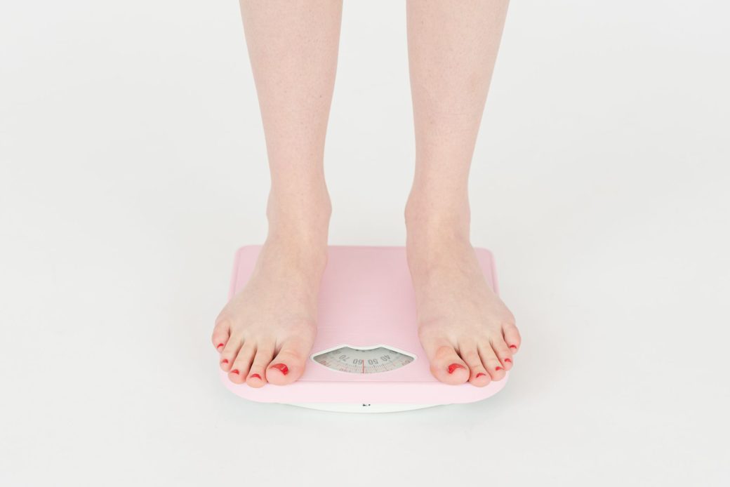 High angle of crop anonymous female measuring weight for control body against white background in studio