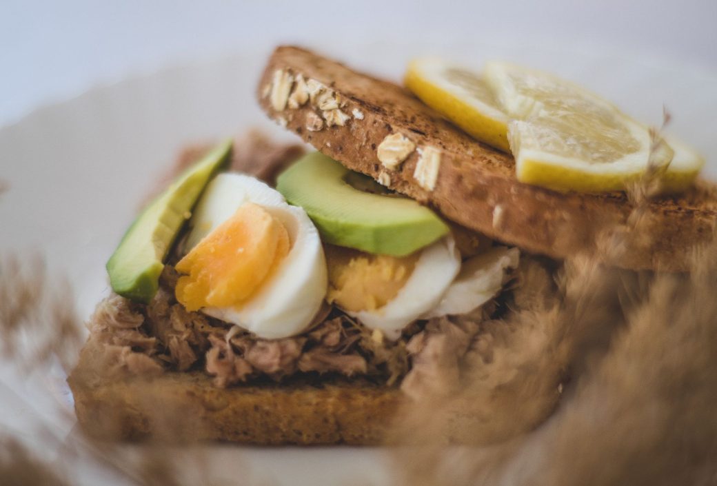 Close-up of a healthy avocado, tuna, and egg sandwich with lemon slices.