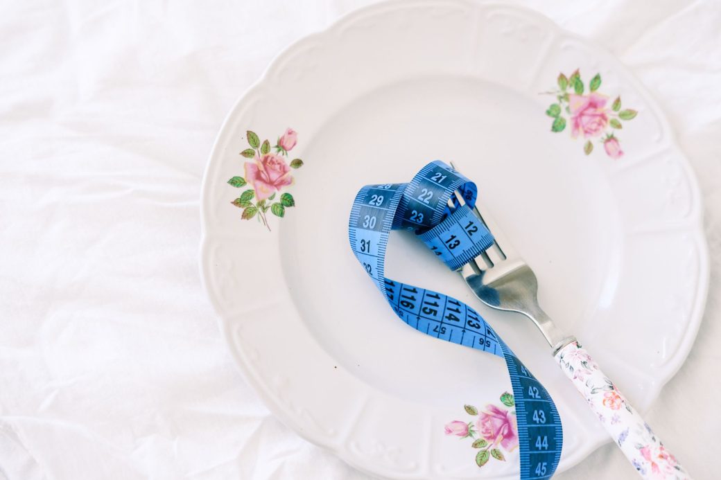 A floral plate with a blue measuring tape wrapped around a fork, symbolizing dieting.