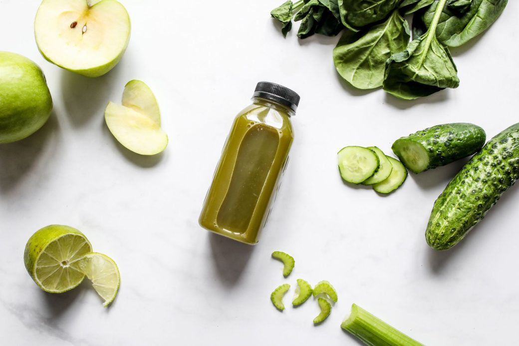 Discover fresh green juice surrounded by spinach, cucumber, apple, and lime.