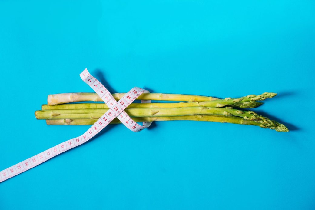 Fresh asparagus wrapped with measuring tape on a vibrant blue background.