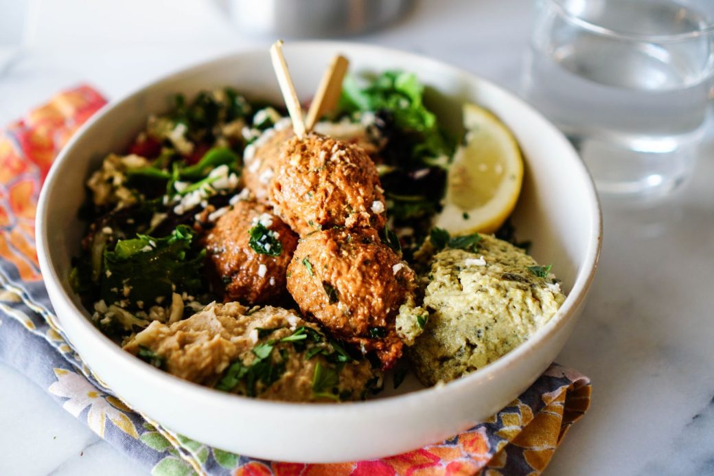 Tasty Mediterranean falafel bowl with fresh greens, a lemon slice, and hummus.
