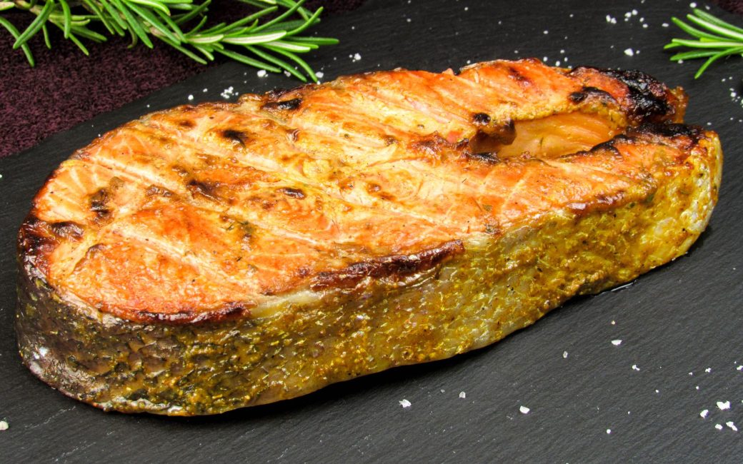 Delicious grilled salmon steak garnished with fresh rosemary on a slate board.
