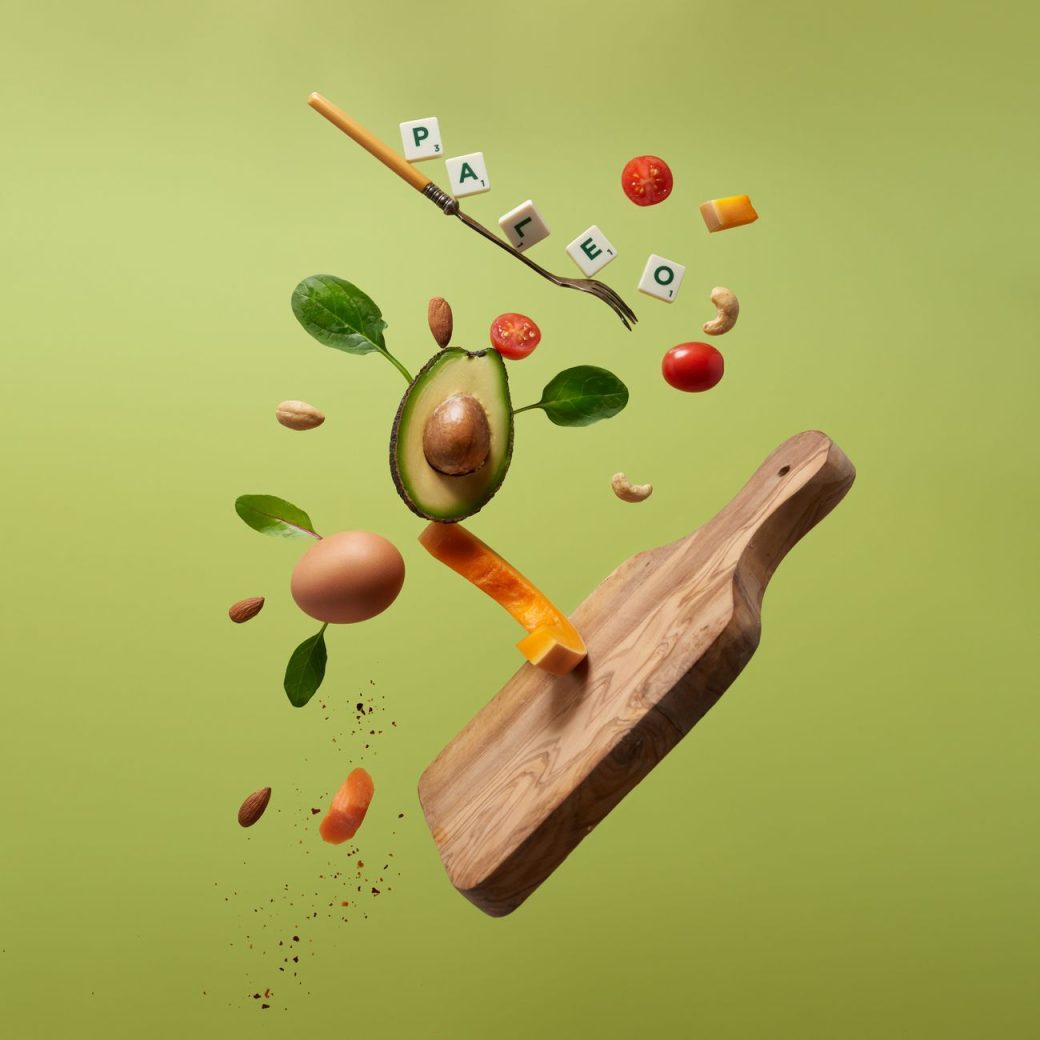 A creative arrangement of paleo diet ingredients floating above a wooden board on a green background.