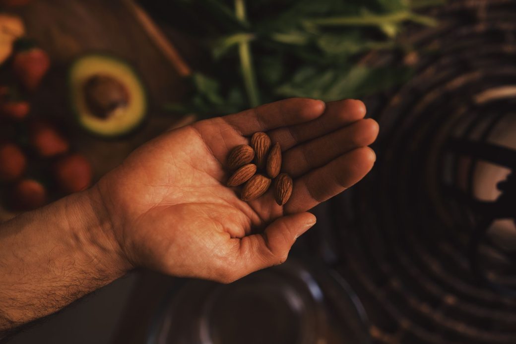Top view of crop hand with pile of raw unpeeled almonds above table with ingredients