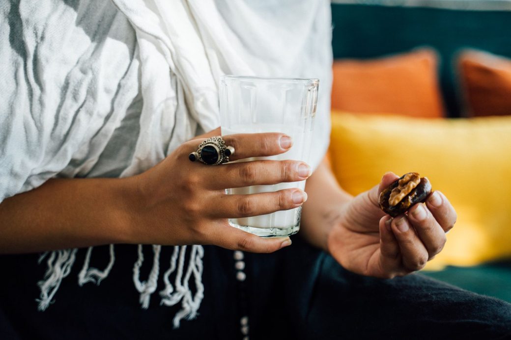 A close-up image showing hands holding a glass of milk and a date, symbolizing Iftar.