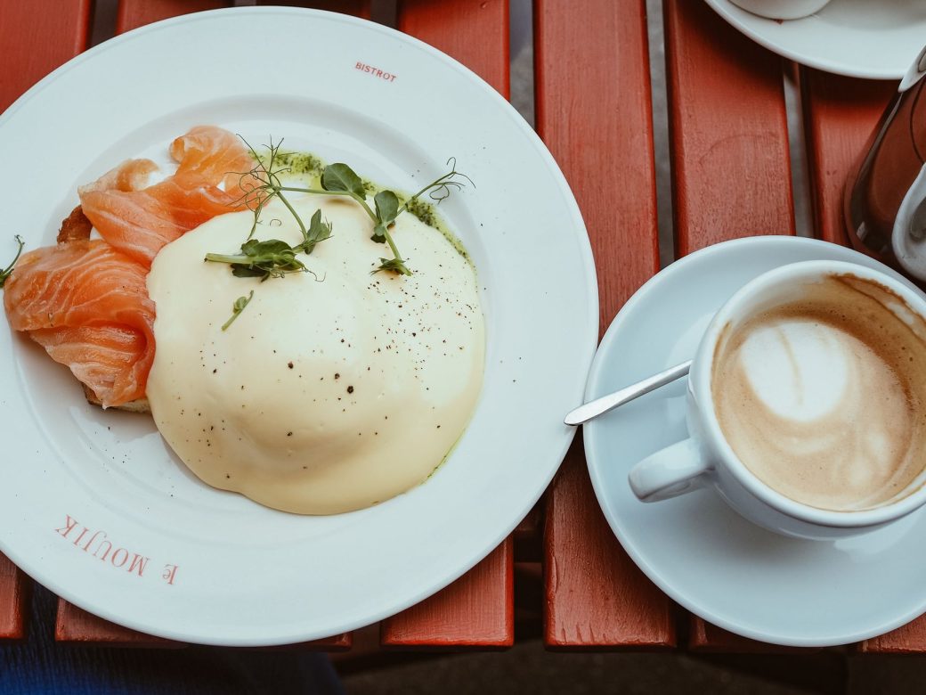 Plate of eggs benedict with smoked salmon and cappuccino on a red table.