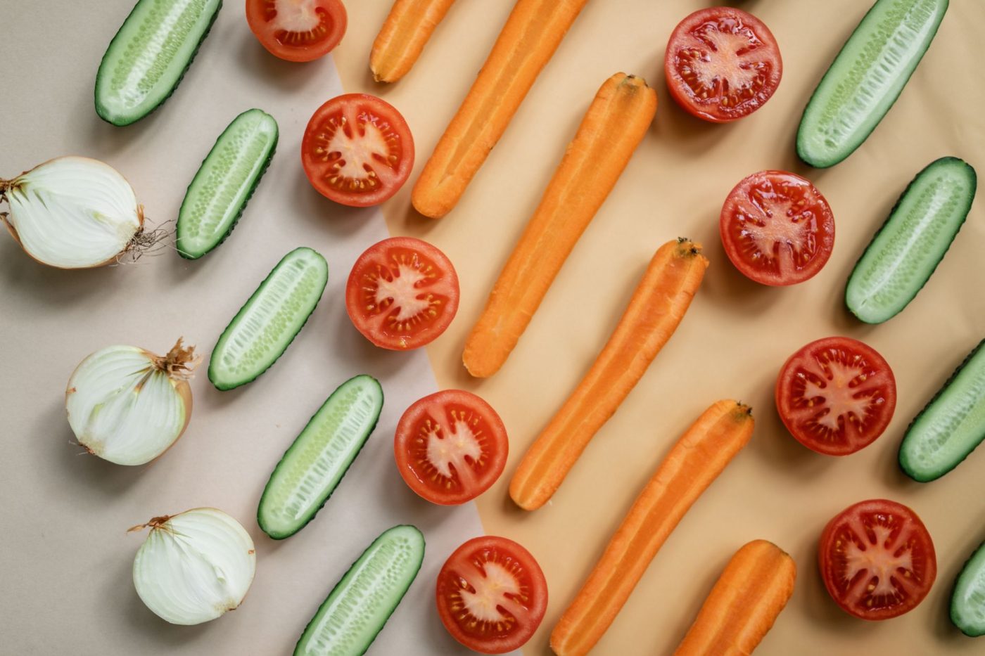 Fresh sliced vegetables including carrots, cucumbers, onions and tomatoes in a flat lay.